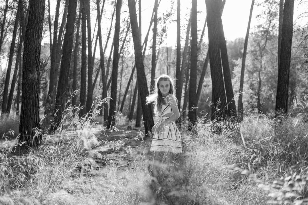 Fotografía en blanco y negro de una niña pequeña de pie en su comunión mirando de lado a la cámara