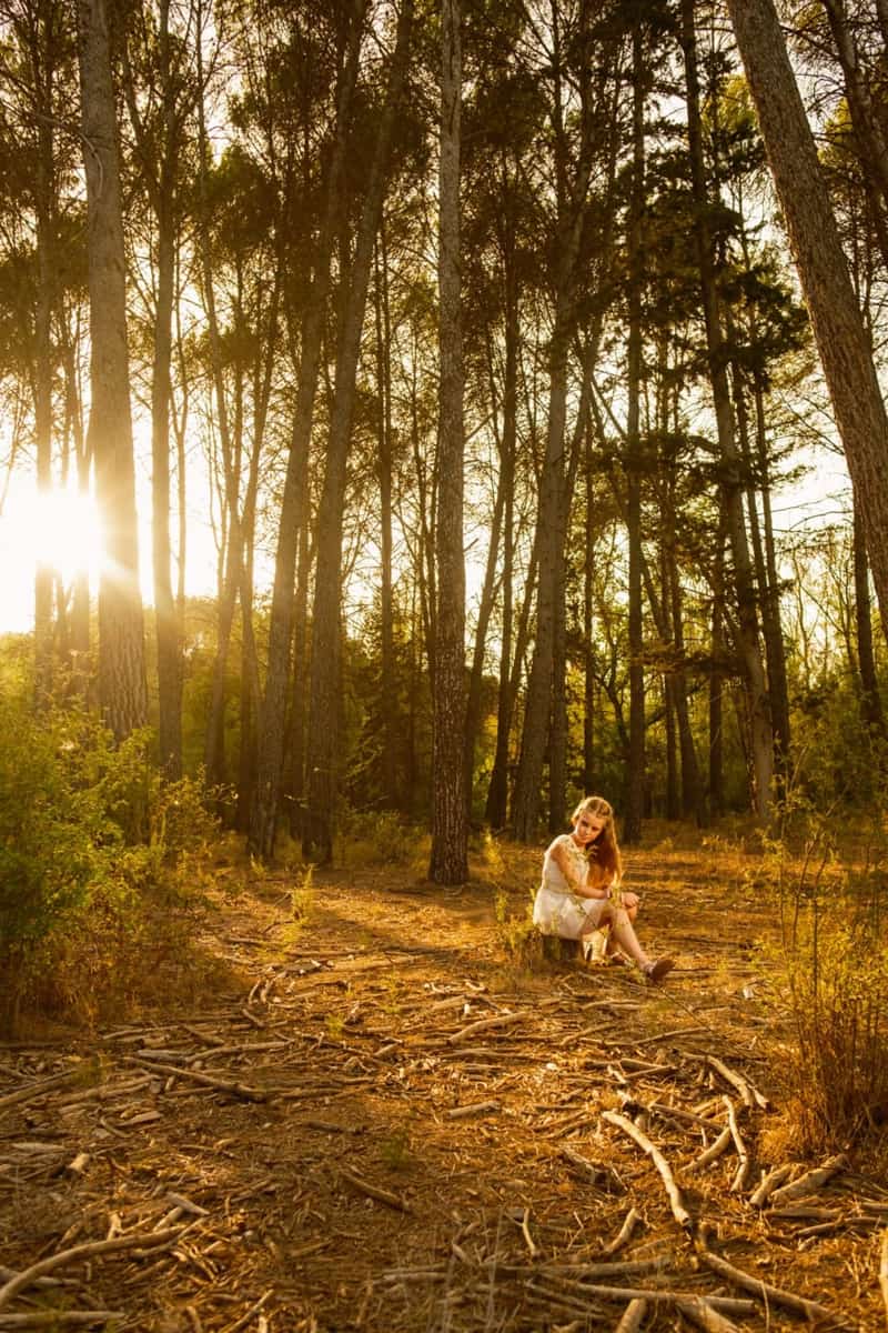 Fotografía de una niña pequeña en su comunión sentada en un tronco en el bosque