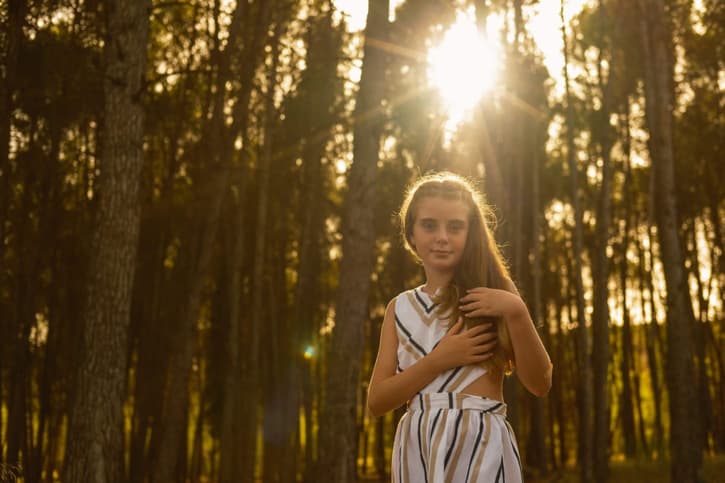 Fotografía de una niña pequeña en su comunión con los rayos de sol penetrando entre los árboles