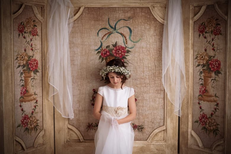 Fotografía de una niña de comunión con una corona de flores mirando hacia abajo