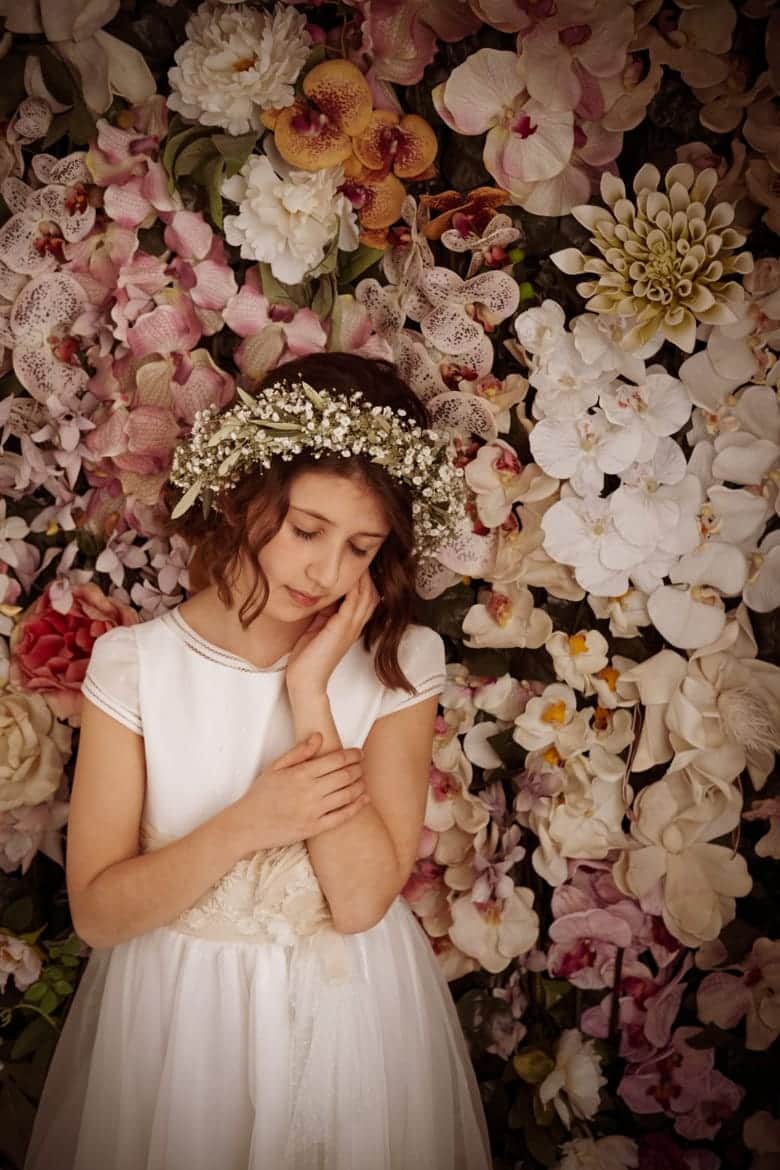 Fotografía de una niña de comunión con una corona de flores apoyando la cabeza sobre su mano