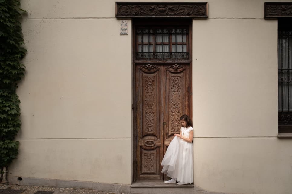 Fotografía de una niña de comunión apoyada en el portal de una casa en Granada