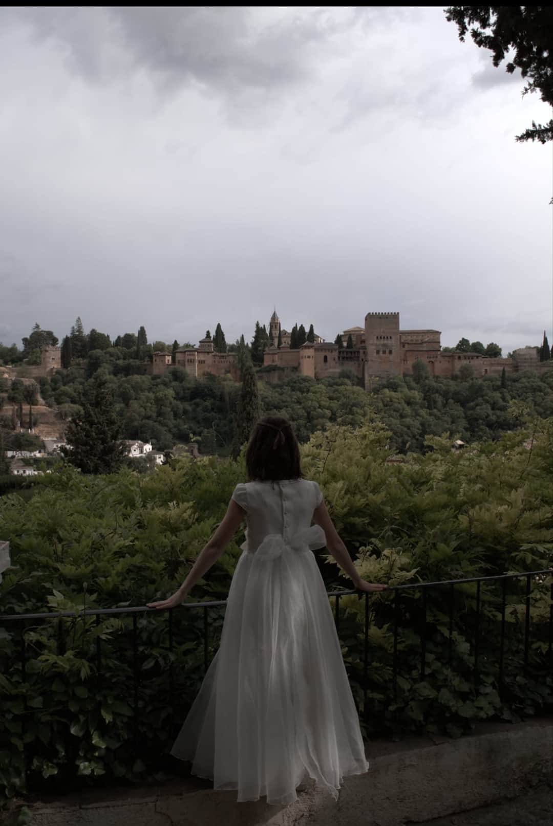 Fotografía de una niña de comunión de espaldas apoyada en una barandilla mirando la Alhambra