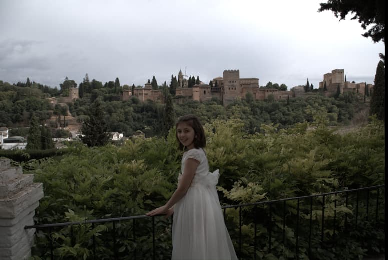 Fotografía de una niña de comunión apoyada en una barandilla con vistas a la Alhambra