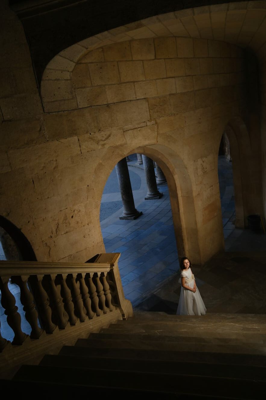 Fotografía de una niña de comunión mirando hacia arriba en unas escaleras antiguas