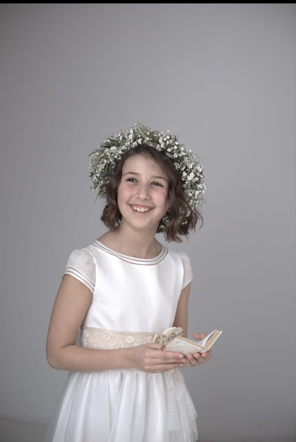 Fotografía de una niña de comunión sujetando una libreta y sonriendo